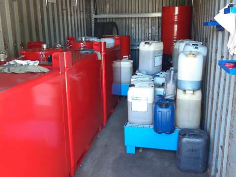 Varastokontti, jossa vasemmalla seinustalla isoja jäteöljysäiliöitä ja oikealla suoja-altaiden päällä olevia pieniä jäteöljykanistereita.