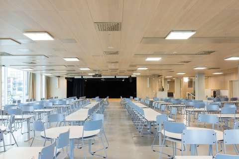 lukion ruokala jossa pöydät ja näyttämö taustalla