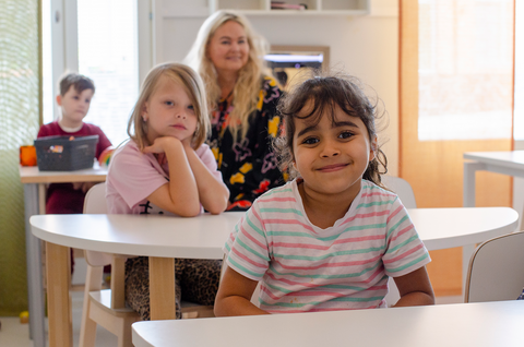 Två barn och en lärare sitter vid borden i förskolan.