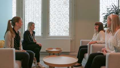 Kuvassa neljä naista keskustelevat nojatuoleissa pöydän ääressä hymyillen.