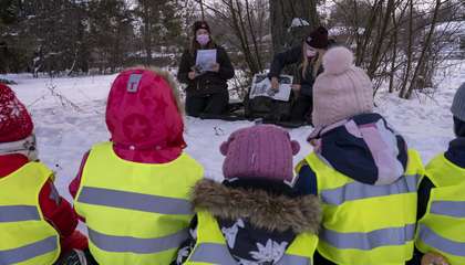 Lapset istuvat maassa ja katsovat, kun ohjaajat piirtävät tarinaa.