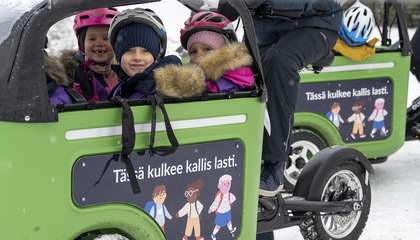 Muksubussissa istuvat lapset katsovat hymyillen kameraan, muksubussin kyljessä teksti: tässä kulkee kallis lasti.