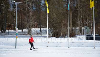 Kuvassa näkyy ihminen hiihtämässä Oittaan laduilla. Taustalla näkyy Espoo liikkuu -lippuja lipputangoissa.