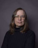 Portrait photograph of a woman wearing a dark sweater against a dark background.