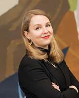 Mustaan pukeutunut henkilö värikkään taustan edessä.