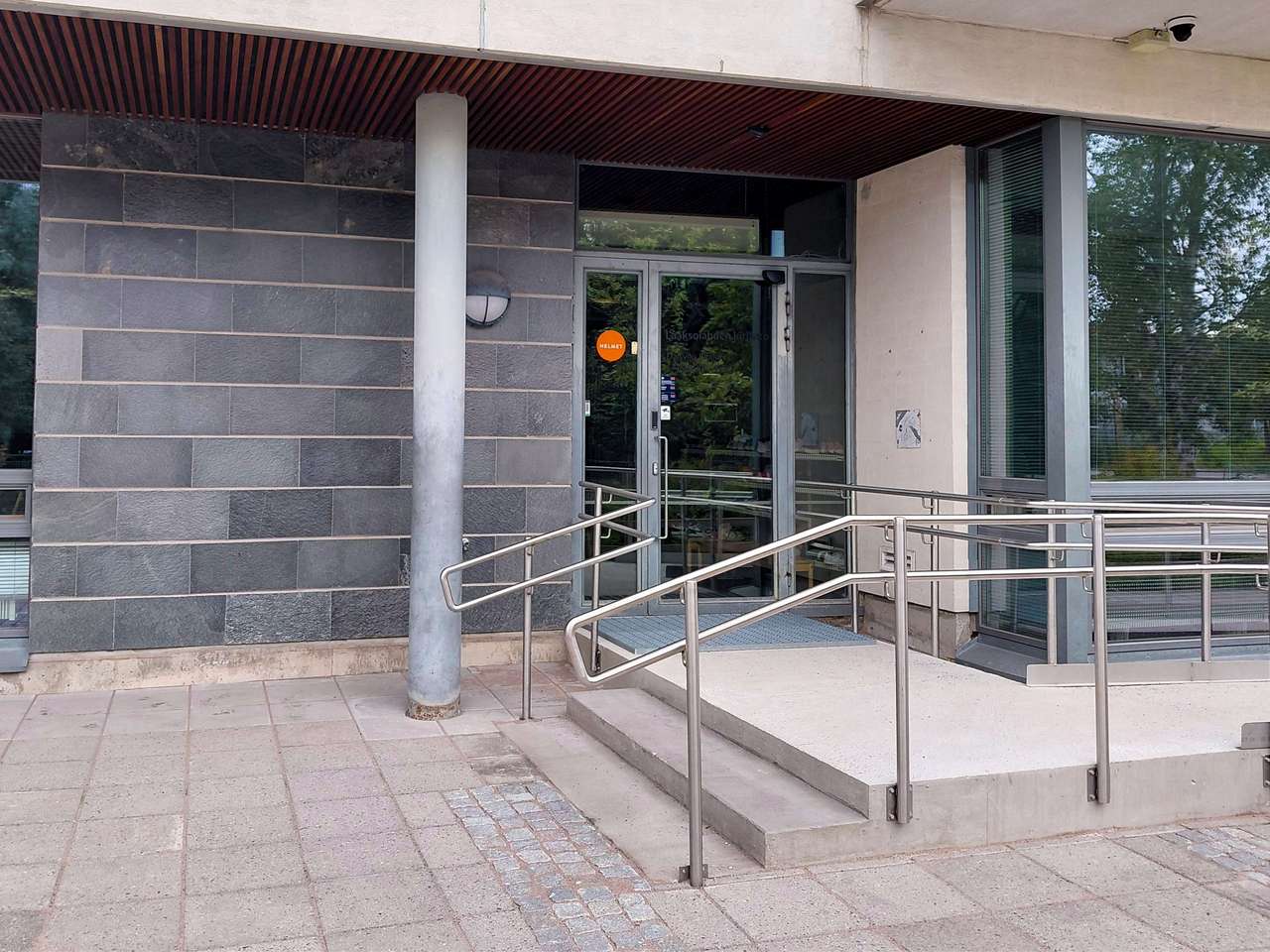 Dörren till Dalsvikshuset. På dörren finns Helmet-bibliotekens orange symbol. Dörren kan nås både via trappor och via en ramp.