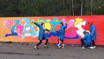 kuva iloisista oppilaista seinän eessä. Värikkääseen seinään on kirjoitettu sana Kartzi.