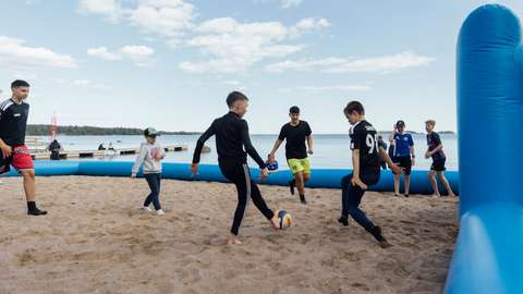 På bilden spelar ett gäng unga killar fotboll på en sandstrand. Planets gränser är luftfyllda.