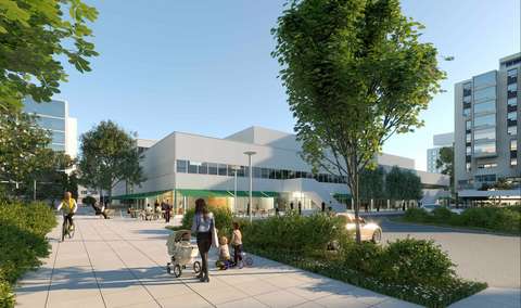 uvan taka-alalla Heikintorin tavaratalo Länsituulenaukion laidasta. Etualalla kävelijöitä ja pyöräilijöitä Heikinkujalla. Pensaiden ja puun takana Länsituulenaukion pysäköintialue autoineen. Heikintoria vastapäätä kuvan vasemmassa reunassa näkyy uusi kahdeksankerroksinen asuintalo.