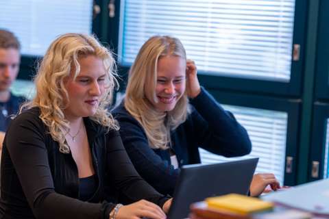 Två flickor sitter i klassrummet och ser på en datorskärm och ser glada ut.