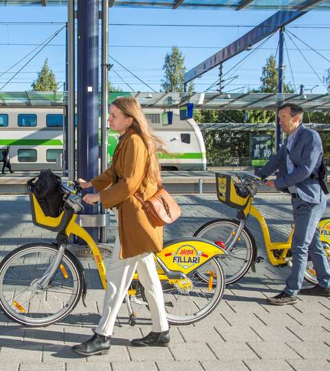 Kaksi aikuista taluttaa pyörää juna-asemalla.