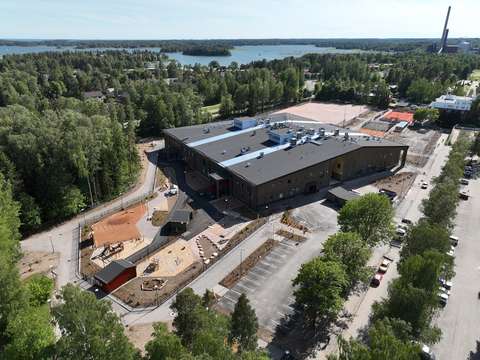 Flygbild av Tiistilän koulu och päiväkoti. I förgrunden syns parkeringsplatser på skolgården och i bakgrunden syns träd och hav.