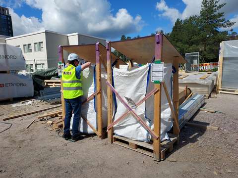 Två stora plastsäckar på en arbetsplats. En person klädd i signalväst kikar in i en av dem.