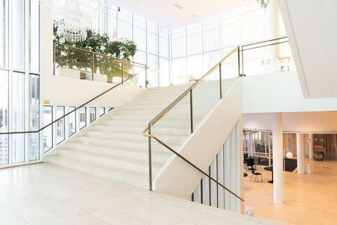 Vaalea, leveä portaikko, joka johtaa aulaan, johon tulvii valoa seinän kokoisista ikkunoista.