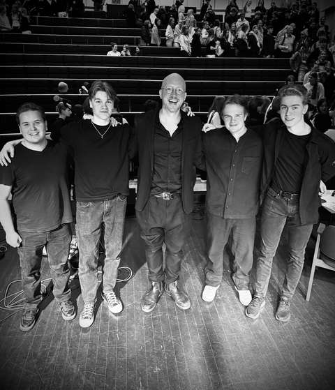 Viisi henkilöä poseeraavat kameralle rivissä.