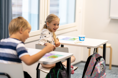 Kaksi hymyilevää lasta istuu luokkahuoneessa pulpeteissaan.