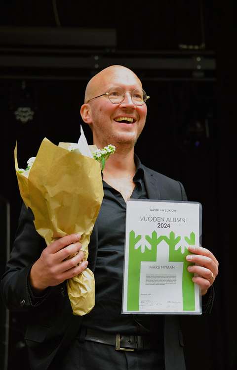 Mies hymyilee kunniakirja ja kukkakimppu kädessä.