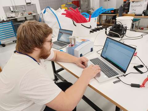 En person sitter vid ett bord framför en dator. Runt omkring finns plaströr i olika färger.