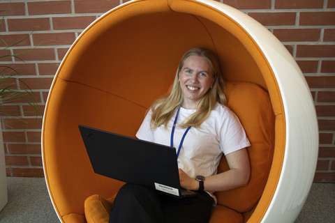 Riina istuu oranssissa, pyöreässä nojatuolissa läppäri sylissään. Hän hymyilee leveästi.