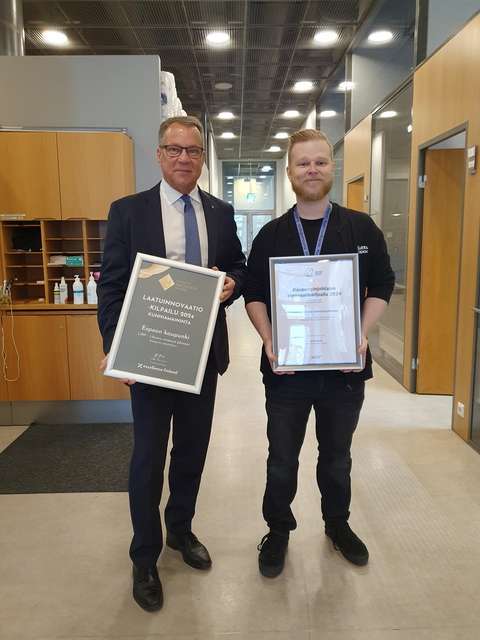Two people standing and looking toward the camera, holding award plaques in their hands.