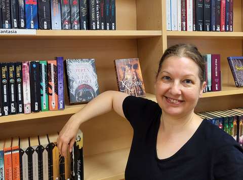 Kirjastopalvelupäällikkö Katariina Lauronen nojaa kirjahyllyyn ja hymyilee kameralle.