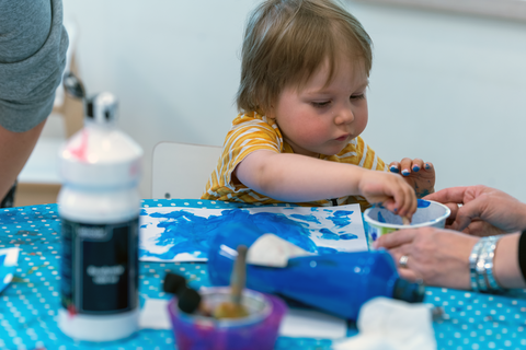 Lapsi maalaa ja aikuinen avustaa