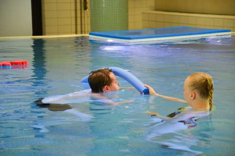 Kuvassa poika ui uima-altaassa sinisen pötkylän ali.