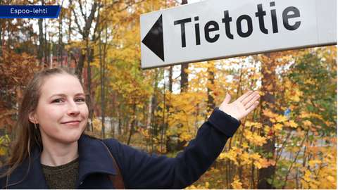 Aurora Salmi katsoo kohti kameraa ja osoittaa toisella kädellä  Tietotien tienviittaa.