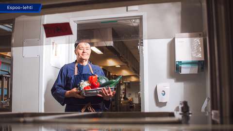 Marjo Sundström katsoo kohti kameraa ja pitää käsissään tarjotinta, jolla on vihanneksia.