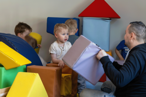 The children and the teacher are building something out of large building blocks.