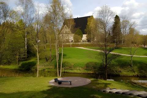 Keskellä kuvaa taustalla on Espoon tuomiokirkko. Etualalla on Espoonjoki ja rannalla oleva kivetty oleskelualue sekä oleskelualueelle johtavat portaat. Kuva on otettu keväällä, kun puut vasta hieman vihertävät.