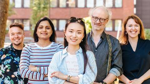 Five people stand outside in a row and smile for the camera.