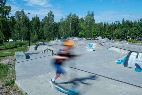 Kuvassa näkyy skeitti- ja skuuttipuisto. Keskellä kuvaa on skuuttaava lapsi.