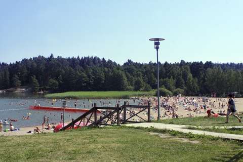 Kuvassa on Oittaan uimaranta kauniina kesäpäivänä. Rannalla on paljon auringonottajia ja uimareita.