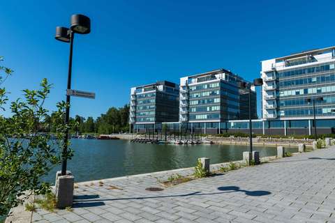 I förgrunden finns en stenlagd del av Strandpromenaden, och havet i Kägeludden. I bakgrunden syns moderna kontorshus.