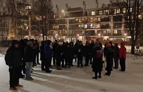 Joukko ihmisiä kerääntyneenä kerrostalojen edessä olevalle lumiselle aukiolle.