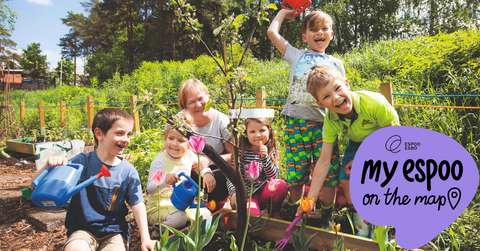 Five children with an adult in a green allotment with gardening tools.