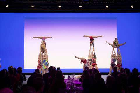 Kuvassa akrobatiavoimistelijat esiintyvät lavalla. Kolme tyttöä tasapainottelee käsilläseisonnassa muiden käsien päällä.