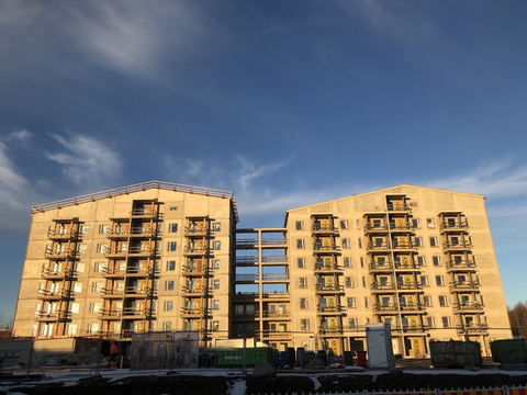 Kaksi harmaata kerrostaloa vierekkäin auringossa, taustalla sininen taivas.