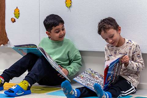 Två förskolebarn sitter på golvet och läser böcker tillsammans.