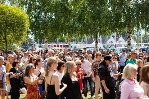 Ulkoilmatapahtuman yleisöä aurinkoisella nurmikkoalueella venesatamassa.