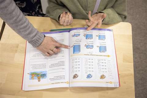 A child is solving problems in the math book and the teacher is giving advice.