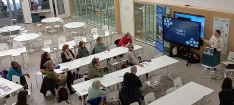 Kouluruokalassa pieni joukko kuulijoita seuraa arkkitehdin esitystä.