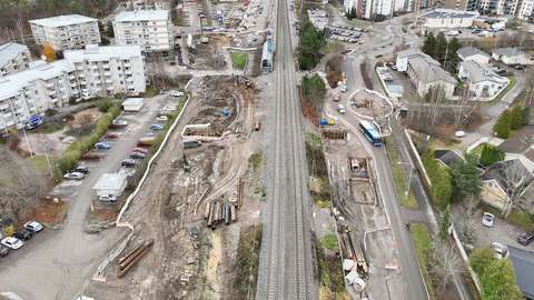 Flygbild av området kring Kilo tågstation. I mitten av bilden löper järnvägsspår och omkring dem ligger en byggarbetsplats. Runt byggplatsen ligger parkeringsplatser, vägar och bostadshus.
