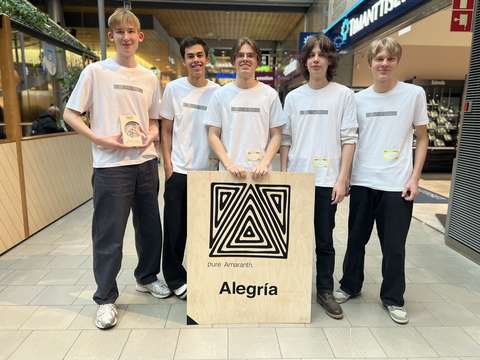 Viisi nuorta on iloisina valkoisissa t-paidoissa. Lattialla keskellä on opiskelijoiden yrityksen kyltti. 