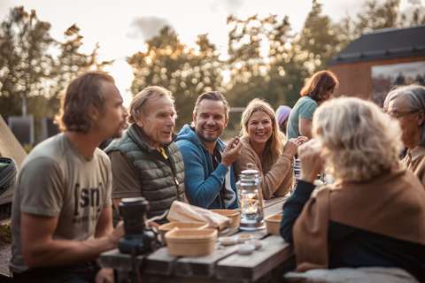 Hymyilevät ihmiset istuvat ja keskustelevat ulkona pöydän ääressä.