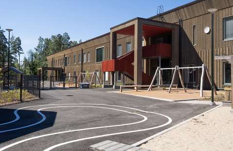 Puinen rakennus, josta lähtee punainen portaikko. Etualalla lasten leikkipaikka.