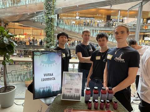 Neljä nuorta on myyntipöydän takana. Pöydällä on pulloja.