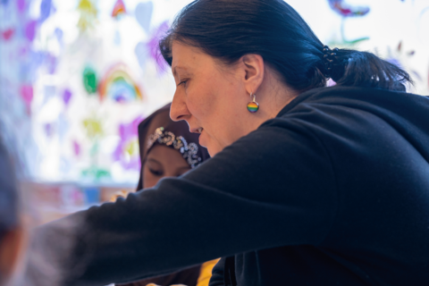 Opettaja istuu ja puuhailee jotakin lasten kanssa pöydän ääressä.