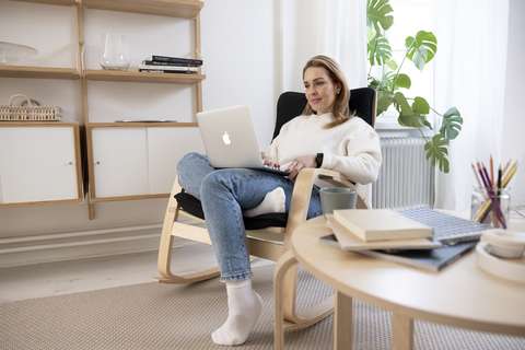 Nainen istuu nojatuolissa kannettava tietokone sylissä.